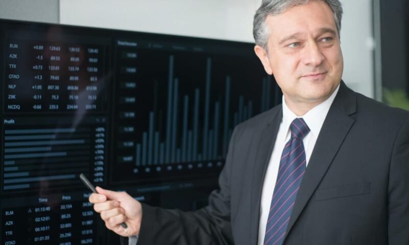 Professional man in suit reviewing financial charts on monitor, showcasing stock market trends.