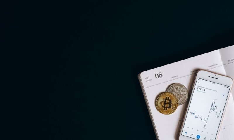 Smartphone displaying cryptocurrency data next to Bitcoin on a calendar offers finance and technology insights.