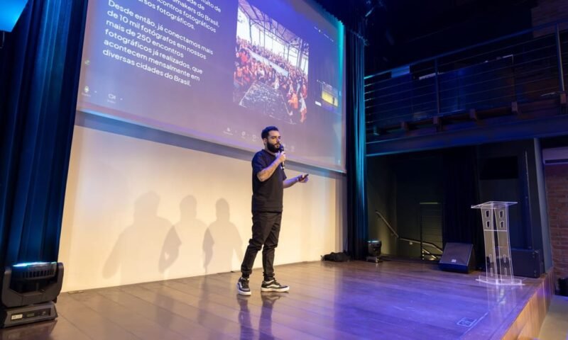 Speaker presenting at a conference with a projected presentation slide on screen.